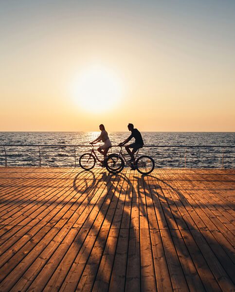 Couple of young hipsters cycling together at the beach at sunrise sky at wooden deck summer time